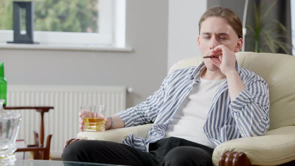 Portrait of Relaxed Wealthy Young Man Sitting on Armchair Smoking Cigar and Drinking Scotch Whiskey