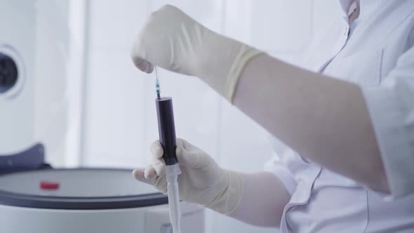 Unrecognizable Nurse in Gloves and White Medical Robe Opening Syringe Filled with Blood. Laboratory