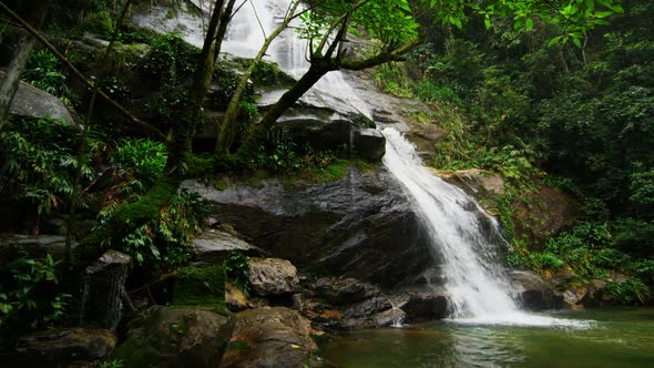 Tracking shot of a jungle waterfall cascading into a deep green pool