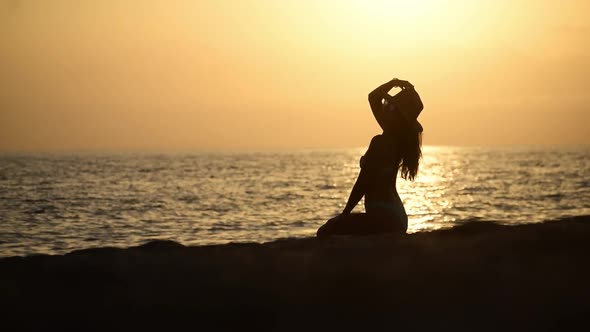 Silhouette of young woman wearing hat relaxing, unwinding at the beach during sunset