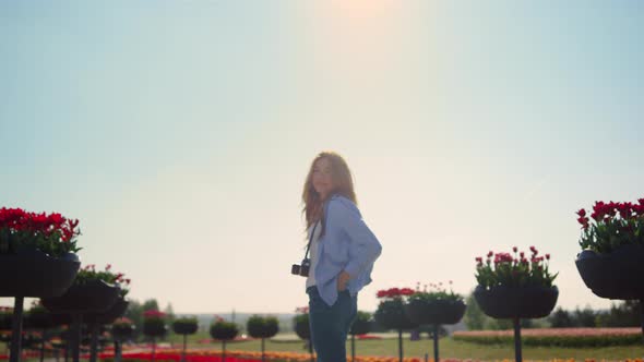 Smiling Girl in Jeans Standing with Camera in Blossomed Spring Park in Sunshine