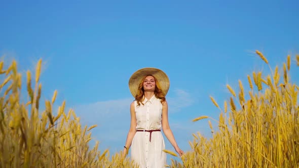 Happy Redhead Girl Walking Among Wheat Ears in Harvest Season