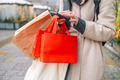 female shopper hand holding red blank shopping bags used phone on the city street  - PhotoDune Item for Sale