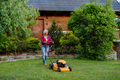 Elderly woman mowing grass with lawn mower in the garden, garden work concept. - PhotoDune Item for Sale