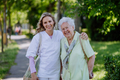 Portrait of caregiver with senior woman on walk in park with shopping bag, looking at caemra. - PhotoDune Item for Sale
