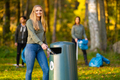 Smiling young woman putting bottle in garbage bin - PhotoDune Item for Sale