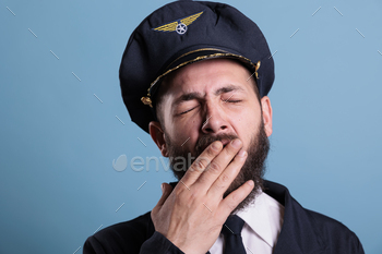 iator covering open mouth with hand. Sleepy aviation academy aircraft captain in uniform with closed eyes front close view