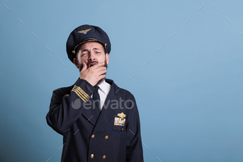 with hand, exhausted aviator. Sleepy aviation academy plane captain in uniform with closed eyes front view, studio medium shot