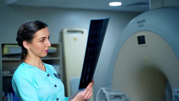 Woman doctor is watching x-ray in clinic. Young female expert holding x-ray photo