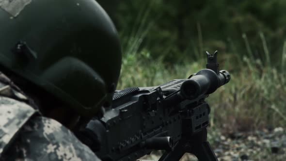 Close view over the shoulder of a soldier as he shoots a belt-fed machine gun.