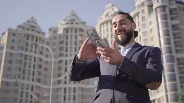 Happy Rich Successful Man Scattering Dollars Outdoors at the Background of Skyscraper. Portrait of