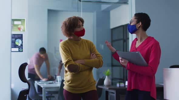 Mixed race female colleagues wearing face masks in office