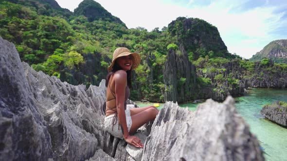 Smiling Woman In Sun Hat Sitting On Rocks Above Hidden Beach