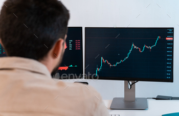 Young caucasian male finance broker analyzing stock graphs while trading from modern home office.