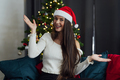Smiling young woman with Santa Claus hat on couch at home - PhotoDune Item for Sale