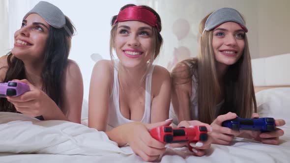 Smiling Young Ladies Lying on Bed and Playing Video Games