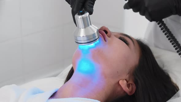Young Brunette Woman Getting Facials  Therapist Using Light Device on Her Chin