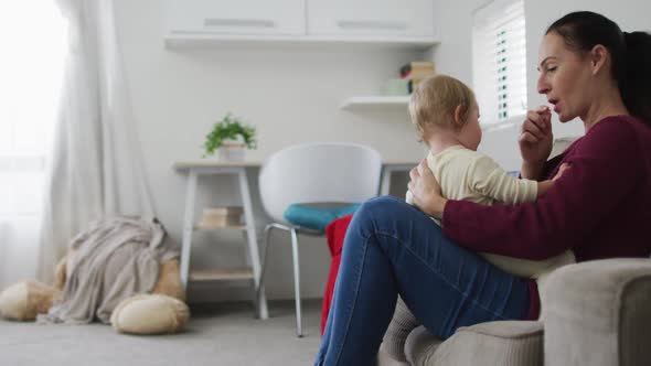 Caucasian mother blowing a whistle while playing with her baby sitting on the couch at home