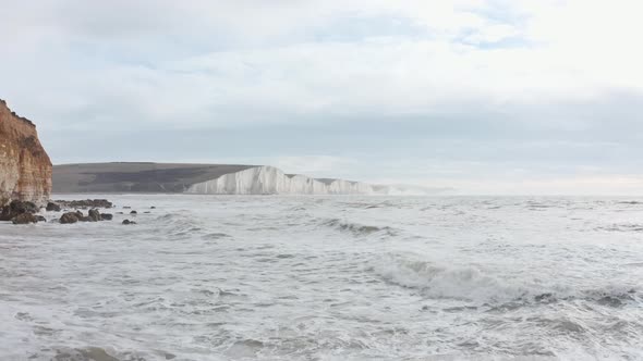 Slow drone shot over rough high tide towards seven sisters cliffs South England