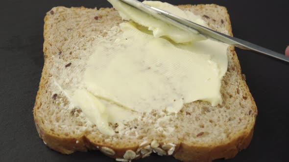 knife puts butter on a slice of cereal bread and spreads it out