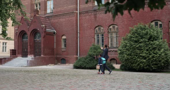 Side View of Guy in Suit and His Son with Backpack Holding Hand in Hand While Walking, Father