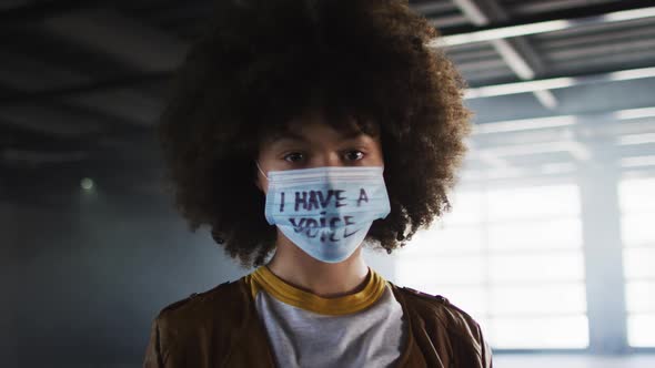 Portrait of african american woman wearing protest face mask gesturing stop sign in empty parking ga