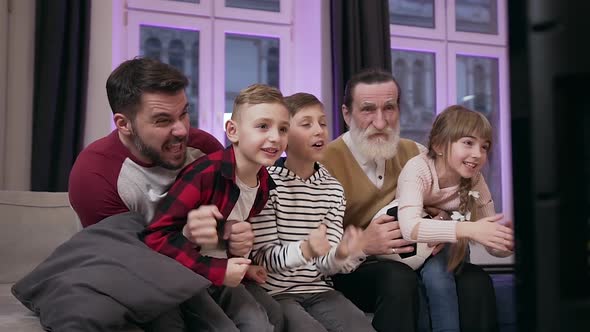 Father and Senior Grandfather with Three Joyful Teen Grandchildren Watching Football Game