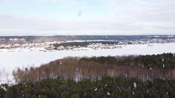 Frozen lake and town in horizon in winter season during snowfall, aerial drone view