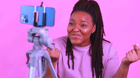 Dark Skinned Woman Laughing and Shooting Social Media Stories in Pink Wall Background