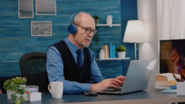 Focused Old Entrepreneur with Headphones Listening Music Typing on Laptop