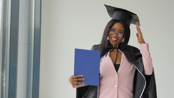 African American Female Graduate in a Classic Suit and Mantle of a Master Stands with a Diploma in