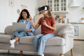Concentrated little teen girl with VR glasses visits 3D metaverse and sits on sofa near mother - PhotoDune Item for Sale