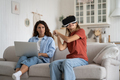 Working from home mother looking strictly at excited little girl daughter in VR helmet playing games - PhotoDune Item for Sale