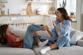 Joyful Caucasian mom in casual clothes and school age girl playing tickling sits on sofa at home - PhotoDune Item for Sale