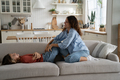 Young European mother tickles daughter to cheer up child lying on couch after hard day at school - PhotoDune Item for Sale