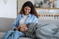 Blissful adorable girl child wrapped in blanket lies on woman mother knees on comfortable home couch - PhotoDune Item for Sale
