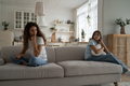 Upset quarreled woman and girl sit on opposite sides of sofa in living room look back at each other - PhotoDune Item for Sale