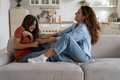 Smiling Spanish woman mom reaching out hands to teenage girl to tickle baby sits on sofa - PhotoDune Item for Sale