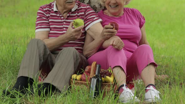 Family Weekend Picnic in Park. Active Senior Old Caucasian Couple Sit on Blanket and Eating Fruits