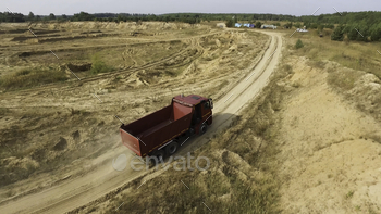 rry with flying dust behind it, industry concept. Empty lorry moving on country road with green forest on the background.