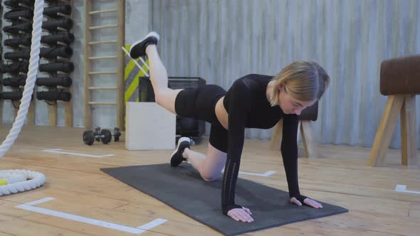 Young Athletic Woman Lifts Her Leg Up Exercise for Abs Core in a Light Gym, Dressed in a Black Top