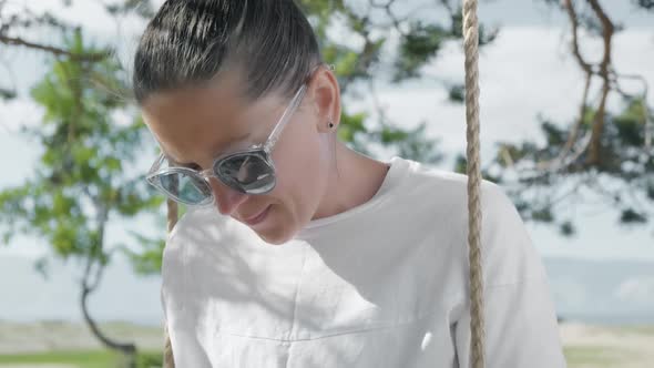 Girl Enthusiastically Uses a Smartphone While Relaxing on a Rope Swing Outdoors