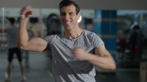 Medium Shot of Smiling Handsome Confident Middle Eastern Man Bragging Muscles Standing in Gym As