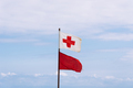 Rescue red cross flag and red flag waving against sky in the beach - PhotoDune Item for Sale