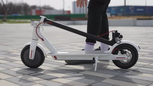 An Unrecognizable Man is Carrying an Electric Scooter