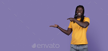 ung guy with long dreadlocks holding something invisible on his hand and pointing at it, isolated on purple studio background, panorama, copy space