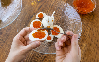  for making stuffed eggs. womens hands cut egg in half and fill eggs with red caviar. canapes with red caviar and quail eggs on a plate