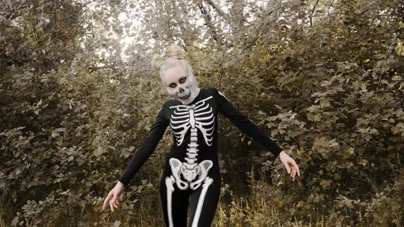 A girl with a scary make-up in a skeleton costume, a mask with rhinestones in a gloomy autumn forest