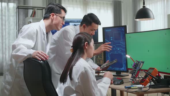 Three Asian Engineers Looking At Motherboard And Talking While Working On Green Screen Computer