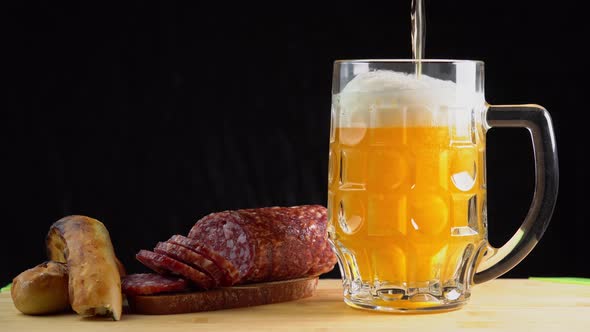 Pouring beer into the glass. Sausage with mug cold craft beer in a glass with water drops